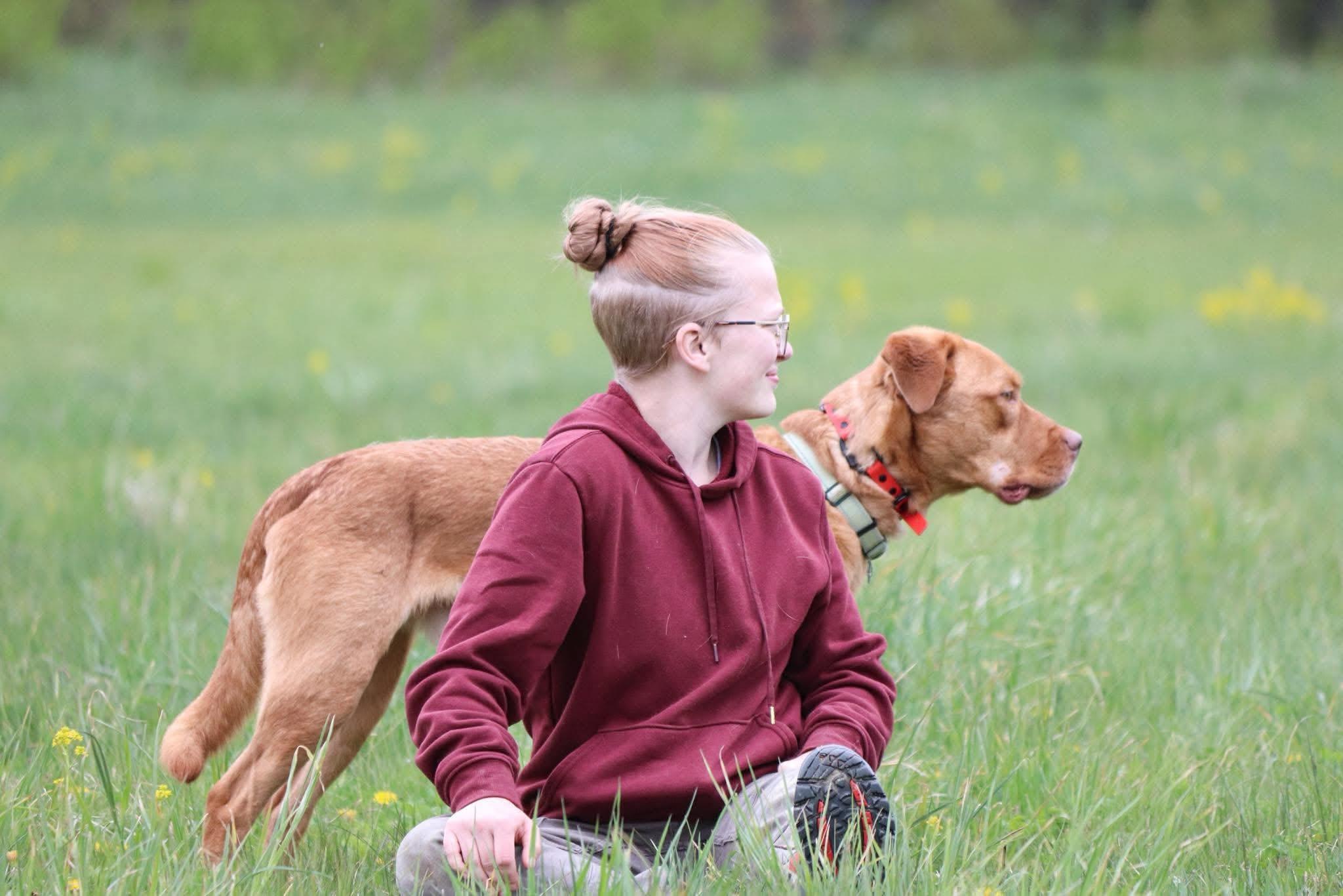 Savannah kneeling in a golden field beside a happy tan dog